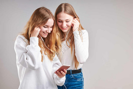 随意的年轻女孩一起收听音乐分享内容乐于观看视频享受聊天与朋友用智能耳机在灰色背景上站立的耳机做手势表情校对Portnoy时髦的简图片