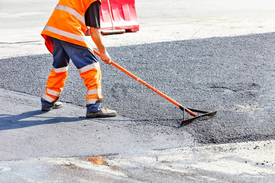 在修复道路时公建筑商在平滑的清新沥青复制空间的背景下用金属水平把新鲜沥青压得达到金属水平道路工人均分配一些沥青在路段周围被红色栏图片