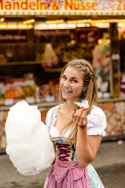 节日穿着传统的Dirndl礼服和棉花糖的漂亮女人在OktoberfestOktoberfest背景中的文字写着bottMande图片