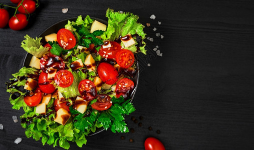 番茄沙拉配有生菜山羊奶酪新鲜蔬菜芝麻种子和橄榄油放在黑木制桌面的板上混合食物夏天图片