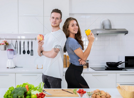 胡萝卜微波手持红苹果的男子和手持黄铃椒的妇女在厨房做健康食物时站立一对微笑的情侣水果图片