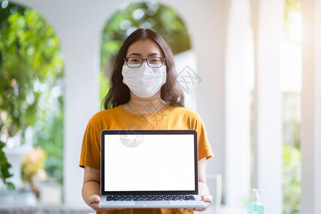 身戴保护面罩的女商业自由职者偶尔举起手来用空白屏幕显示笔记本电脑防止COVID19传播的概念大学生嘲笑图片