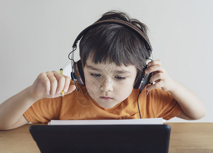 搜索小学生戴耳机听老师在桌上教授线课程小男孩在数字平板上学习和做作业社交距离在线教育和远程学习概念疏患病的图片