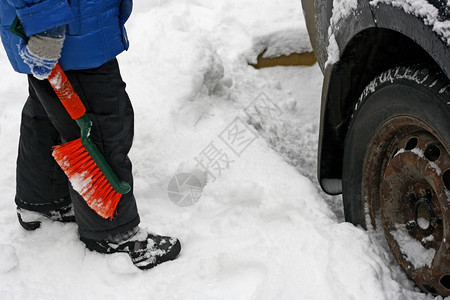 霜值得一名儿童站在汽车旁边用老生锈的轮子拿着橙色刷擦洗车上的雪景象持有图片