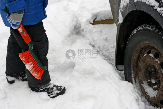 霜值得一名儿童站在汽车旁边用老生锈的轮子拿着橙色刷擦洗车上的雪景象持有图片