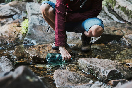 女人在山上漫步时用水瓶装河流里的水图片