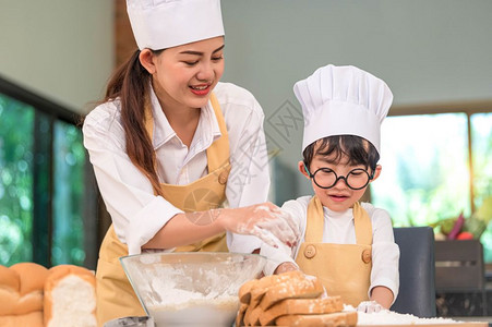 美丽的女人和可爱小亚洲男孩带着眼镜厨帽围裙和在家中厨房里打烘烤面包机风趣自制食品和面包泰语教育和学习概念泰国童年玩图片