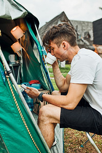 温暖的年轻人喝着咖啡坐在帐篷前早上的青少年在暑假周末旅行期间享受自由时青年男子喝着咖啡早上坐在帐篷前男孩喝着咖啡真实的徒步旅行者图片