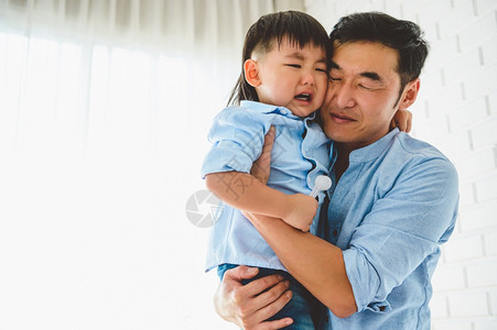 男生亚洲日本父亲在家的卧室里抱着和安慰哭泣的儿子窗户和白色帘背景人们在Covid19或冠状流行中的生活方式健康检疫沮丧的爱图片