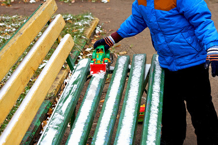 衣服点缀自然寒冷季节的儿童游戏部分是小孩的画面站在被雪覆盖的木板凳旁孩子用玩具挖土机从板凳上扫清雪图片