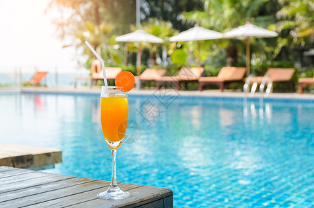 玻璃健康木桌上的橙汁杯子配有游泳池对面的桌椅上橙汁在户外游泳池夏季热带假日概念的木桌上用鸡尾酒杯中的胡萝卜片配有橙汁和胡图片
