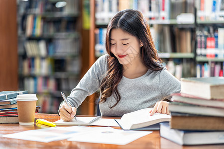 亚洲青年学生在大图书馆或群落阅读和做功课书架背景的木制桌子上有各种书本和文具回学校后读书架背景上的各种书籍和文体或者东盟曼谷图片