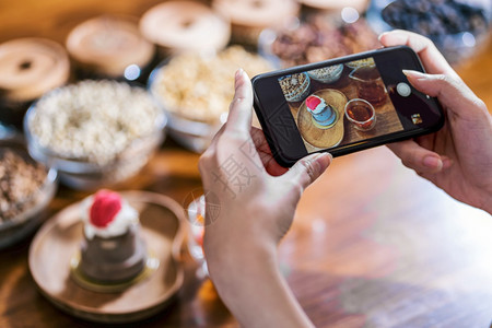 闭合移动电话拍摄蛋糕面包店的照片蜂蜜在咖啡店和餐馆的木桌上配有咖啡壶的蜂蜜甜点以及用于社交网络概念的咖啡时间潮人蜜糖所有者图片