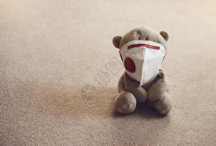 面具晚上医疗的泰迪熊身戴防污染或的护面罩坐在地毯上夜光照亮独坐的LonelyTedddy低基灯光拍摄防止和疾传播的概念图片