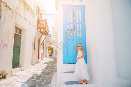 岛在Mykonos的Mykonos穿着外装的小可爱女孩在典型的希腊传统村落街道上有白色的墙壁和多彩大门建筑物人们图片