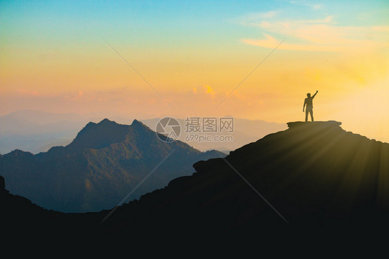 日落时一个手举起欢乐的男子在山顶上轮廓在日落时努力和成功的概念自由常设攀登图片