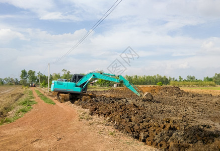 行业现代挖土机正在掘水稻田附近的池塘储存夏季用于农业的水复制空间前视线方进行土掘工作在稻田附近挖掘池塘土方工程碎石图片