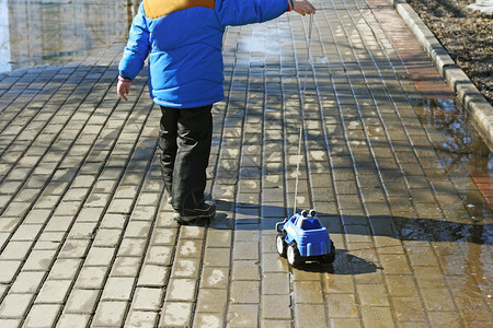 孩子在公园散步男孩穿过水坑拉着玩具车的绳子上路娱乐一种图片