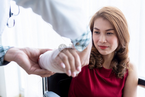 男医生有包护士的绷带在一名女病人的手臂上用模拟压力测量仪穿戴手臂并配有类似压力测量仪以更好地愈合病情医疗的治师步行图片