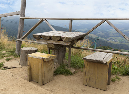 木制的车轮古老木质气候表和三张粗糙的简易椅子在山地景观背下在山上滑雪升起的顶层休养以喀尔巴阡山顶的粗木板桌和椅子的形式临时休息区图片