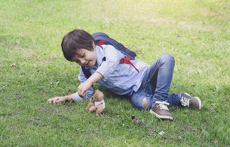 小可爱男孩背着包躺在草地上与Teddy熊在公园玩耍快乐的孩子带着微笑脸在春天或夏和季的户外玩具游戏老的最好白种人图片