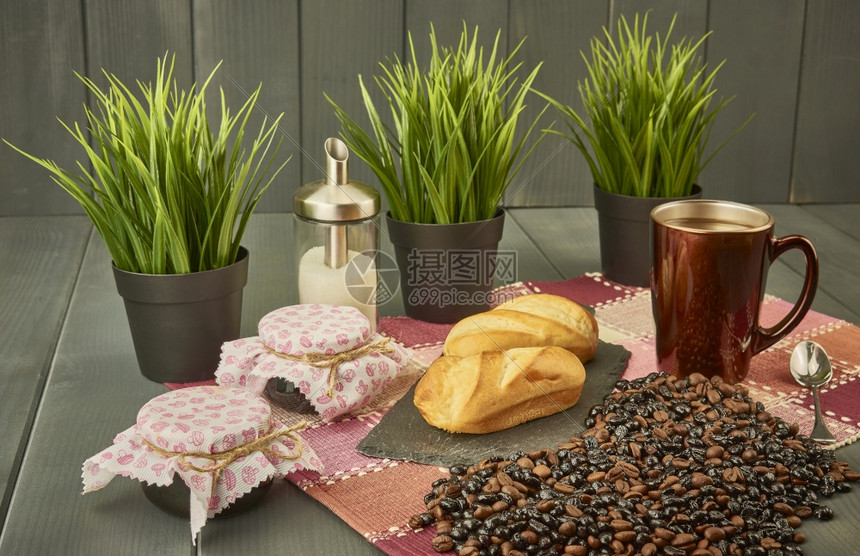 健康豆早餐加咖啡和牛奶面包蜂蜜果酱糖以及天然和烤咖啡的样本配有三株植物灰色木制背景和用红度调料的桌布装饰天然和烤咖啡因图片
