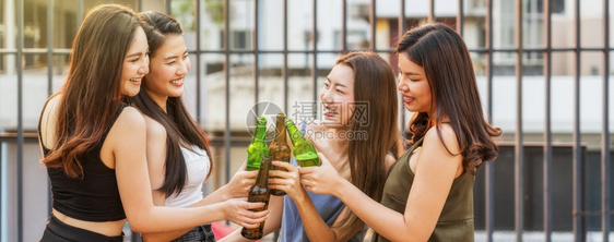 欢乐亚洲女孩朋友团体在日落时市中心酒店或夜总会的屋顶上庆祝和欢周日或年度晚会概念中与啤酒瓶一起庆祝和欢乐享受户外派对图片