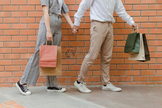 男子穿着浅棕色裤和白鞋左手背着购物袋握身穿灰色短裤和黑鞋子的女手买跑步松弛图片