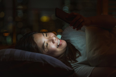 卧室闲暇利用智能手机在社交网络或视频会议电话上睡觉和使用智能手机与她的爱人在夜里模糊城市的床上面对时间生活方式和放松概念在夜间睡图片