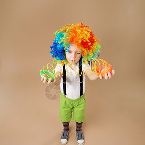快乐的小丑男孩戴着大彩色假发穿着小丑的男孩弹奏着春天的一幅童子肖像在宽角镜头上拍摄生日男孩运动白种人乐趣图片