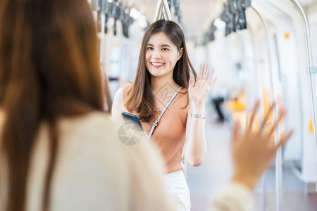 火车韩国人身戴外科面具的亚洲年轻女乘客在Covid19疫情爆发社会动荡与新常态概念等大城市旅行时用手挥向地铁列车朋友打招呼关心图片