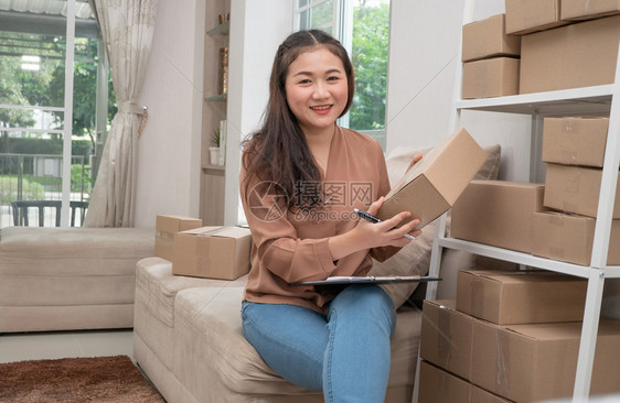 一种年轻创业者坐在沙发上家工作她微笑着并拿一个包装箱用于撰写客户地址信箱发送货物在线销售小企业主概念一小型商业所有者概念人购物图片