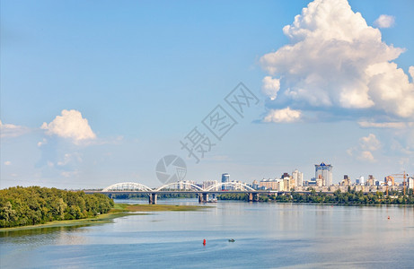 风景优美宿舍在宽度的Dnipro河水面上大云层被阳光照亮浮在蓝色天空中紧绕白色铁路桥和基辅新的住宅区复制了空间Dnipro河附近图片