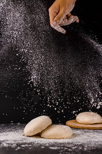 过程面粉和在中间的黑色背景手在面包上撒着粉包子上也喷满了面粉营养包师图片