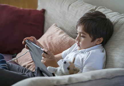 种族坐在沙发上看手机卡通的男孩在互联网上使用手机学习课的校儿童家庭教育远程习在线教育概念等坐落在沙发上的男孩生小工具图片
