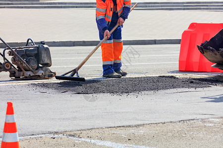 更新机器等级道路建筑商在一条震动板和部推土机的桶子上将部分沥青平配成路面用一根木层以橙锥和红色栅栏围起来的公路段有木层道建筑商平图片