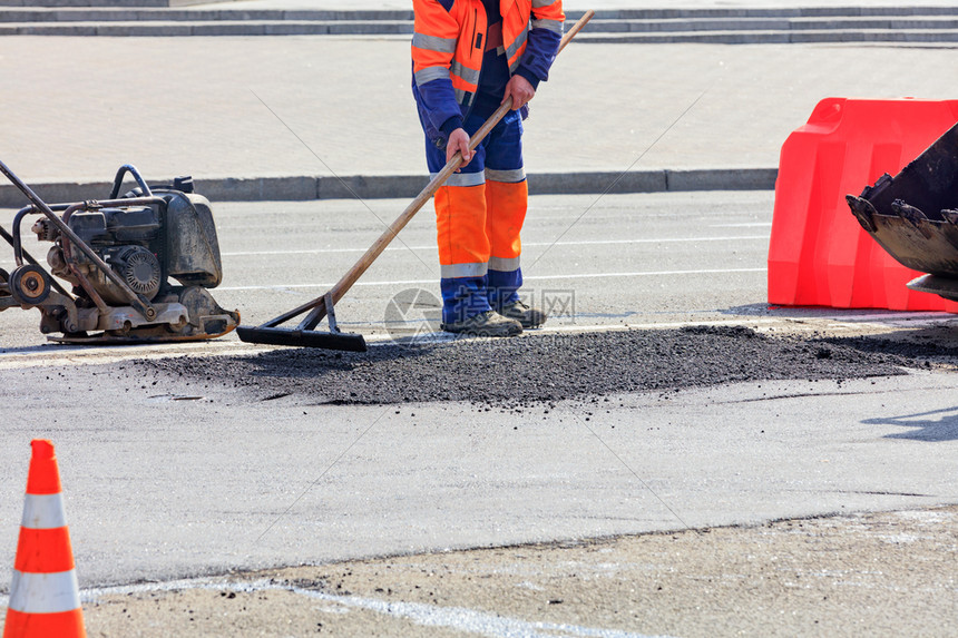 更新机器等级道路建筑商在一条震动板和部推土机的桶子上将部分沥青平配成路面用一根木层以橙锥和红色栅栏围起来的公路段有木层道建筑商平图片