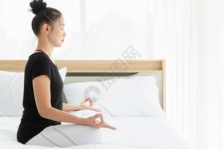 锻炼正在做穿着运动服的有吸引力亚洲妇女在白卧室床上练习冥想瑜伽在晨间保健概念中完成Pose或Siddhasana的平静和放松与瑜图片