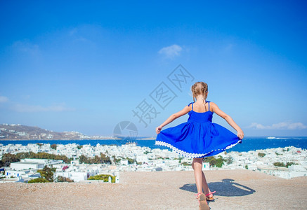 假期希腊语窗户穿着蓝裙子的女孩在户外玩得开心在典型的希腊传统村落老街上看到Mykonos可爱的小姑娘图片