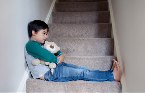 暴力情绪化的独自坐在楼梯上与泰迪熊同坐的萨德阿西安男孩带着悲伤的脸看哀孤独孩子不高兴回到学校沮丧的男孩坐在楼梯角落里家庭图片
