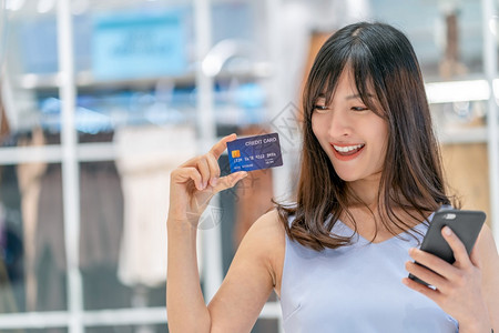 行业亚洲妇女利用信卡和移动电话在百货商店通过服装背景技术钱财包和网上支付概念信用卡模型在线购物亚洲妇女使用信卡和移动电话在服装店图片