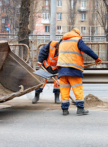 行业身穿明橙色反射制服的道路工人使用铲子清除各行道间的残块并将其装入一个平板桶垂直图像中道路工人将之间积聚的肮脏沙子铲到平板桶垂图片