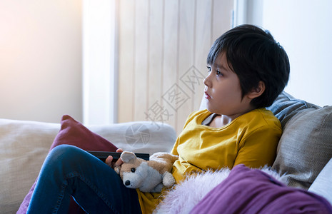 孩子坐在沙发上拿着遥控器坦率的矮个男孩在家放松看电视活跃的孩子在暑假放学时社交距离在线学习教育肖像自新冠图片