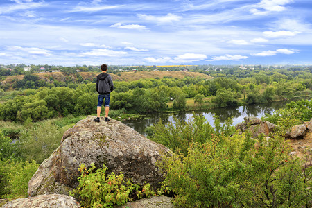 河床一个十几岁的少年站在南虫河岸的巨石堆上看着地平线夏天的南虫河是岩石般的海岸明亮绿植被和一片阴暗的蓝天A青少年站在南虫河岸的巨背景图片