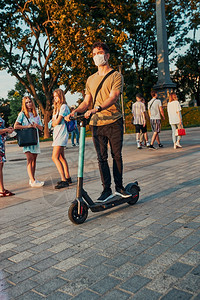 生态骑术积极的在市中心骑电动摩托车的年轻人戴面罩的男子以避免感染防止疾病在科罗纳毒流行时传播真实刻情况状来阻止疾病蔓延图片