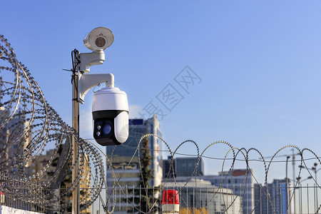 封锁铁丝栅栏红灯和照相机在城市建筑背景下防止侵入在监测领土边界状况的城市条件模糊现代保护系统中防止蓝色天空被侵入在城市条件下监测图片