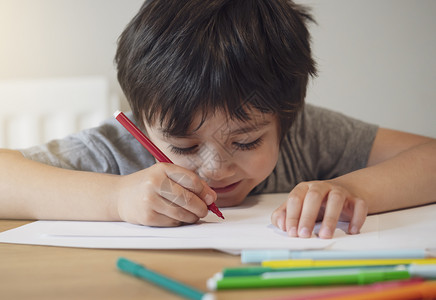 有创造力的小学生坐在桌子上做作业的选择焦点快乐的孩子拿着红笔在白纸上写字或画小学和家庭教育理念严肃的背部图片