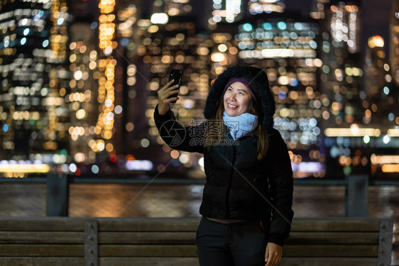 冬季西装亚洲女使用智能手机自拍在东河背景美国市区的纽约风景相片模糊的地方拍摄职业概念是在美国市区的东河背景旁人阅读市心图片