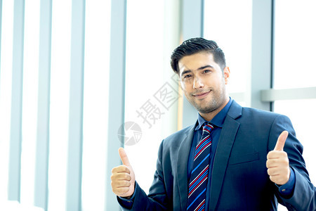 离开充满欢乐的商人样板穿着微笑装的样子在镜头上举起拇指展示与办公室背景相比的成功经验请留下写描述文字的复制空间笔记本电脑越过图片