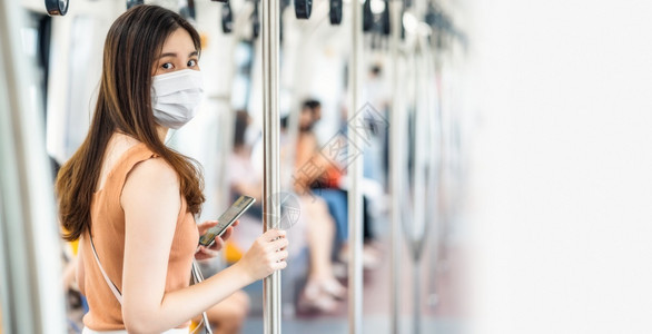 年轻亚洲女乘客在Covid19爆发感染和大流行病社会动荡和新常态概念大城市旅行时身戴外科面具看地铁火车照相机的摄影年轻亚洲女乘客图片